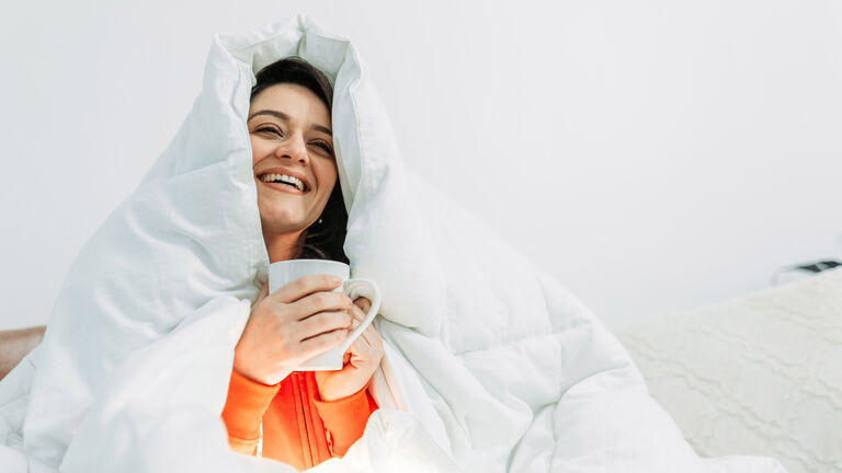 Young woman having coffee under the duvet