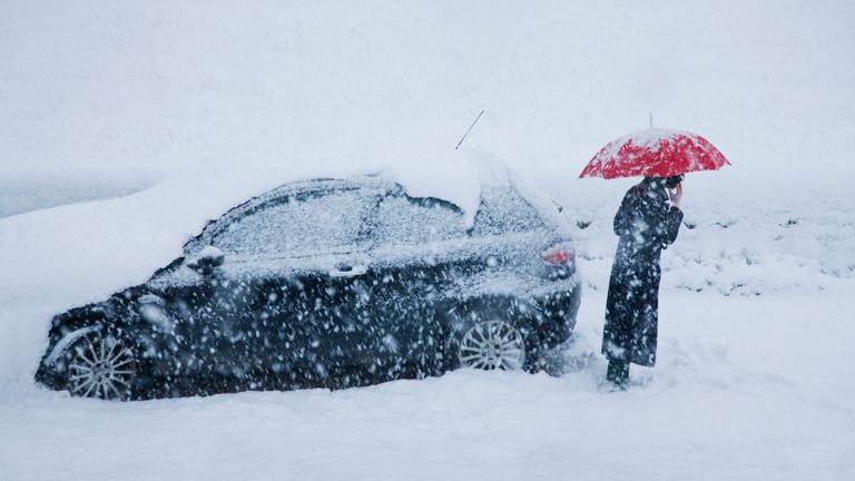 woman on mobile alongside car in a snow drift
