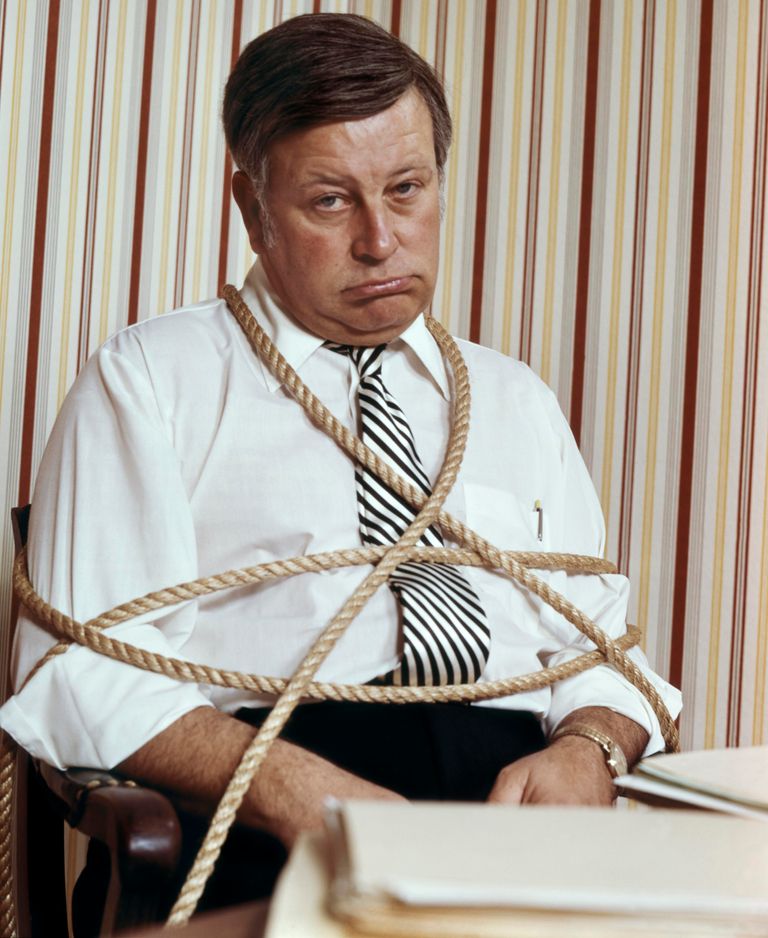 https://www.gettyimages.com/detail/news-photo/1970s-man-in-office-tied-with-ropes-to-his-chair-by-desk-news-photo/1257775282